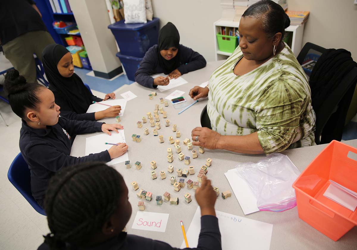 HSA Teacher smiles while kneeling beside a young student in a classroom setting.